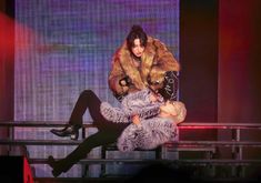 two people sitting on top of each other in front of a stage