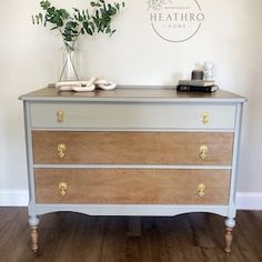 a white and gold dresser with flowers in a vase next to it on top of a hard wood floor