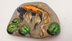 a painted rock with a goldfish and waterlilies on it's side