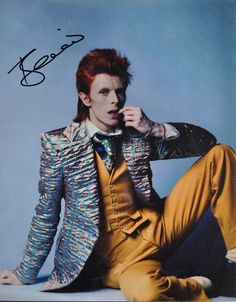 a man with red hair sitting on the ground wearing yellow pants and a colorful jacket