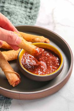 a person dipping sauce onto some food in a bowl on top of a metal plate