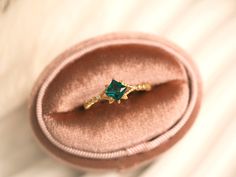 a ring with a green stone in it sitting on a velvet box, close up