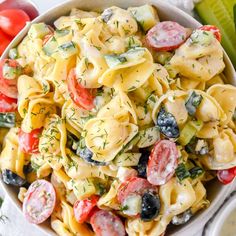 a bowl full of pasta salad with tomatoes and cucumbers