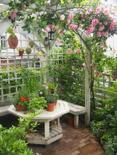 a white bench sitting under a trellis covered in pink flowers and potted plants