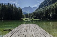 a wooden dock sitting on top of a lake surrounded by trees and mountains in the background