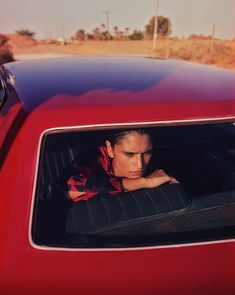 a woman sitting in the back seat of a red car with her head out the window