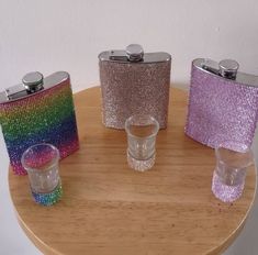 four different colored flasks sitting on top of a wooden table next to glasses