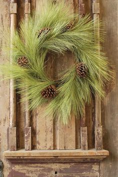 a wreath with pine cones and green grass is hanging on an old wooden door frame