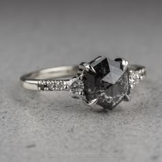 an engagement ring with a black diamond surrounded by white and rose gold diamonds on a gray surface