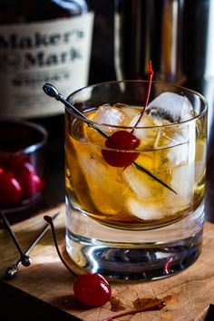 a glass filled with ice and cherries on top of a wooden cutting board