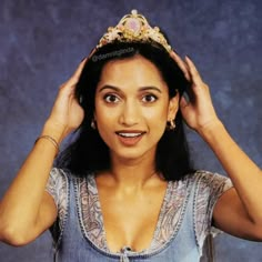 a woman with a tiara on her head posing for a photo in front of a blue background