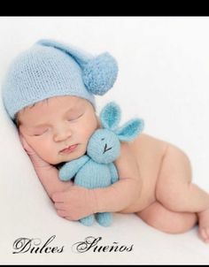 a baby sleeping with a stuffed animal in it's arms and wearing a blue knitted hat