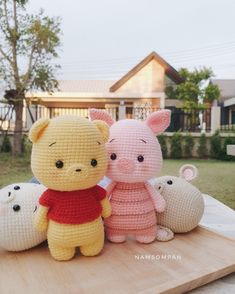 three crocheted winnie the pooh stuffed animals sitting on a wooden board in front of a house