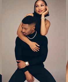 a man holding a woman on his back while she is wearing a black dress and pearls necklace