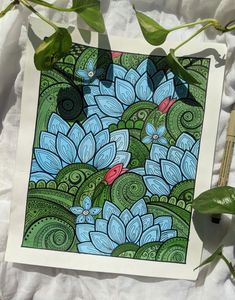 an art work with blue flowers and green leaves on a sheet of paper next to some scissors