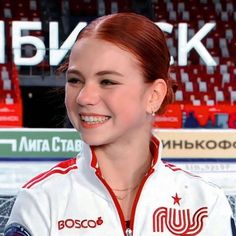 a woman with red hair smiles at the camera in front of an ice hockey arena