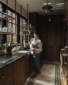 a woman standing in a kitchen next to a sink and window with potted plants