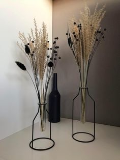 two vases with dried flowers in them on a table next to a bottle and wall