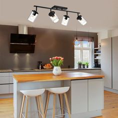 a kitchen with three lights hanging from the ceiling and two stools in front of it