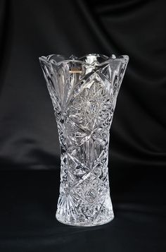 a glass vase sitting on top of a black table next to a black cloth covered wall