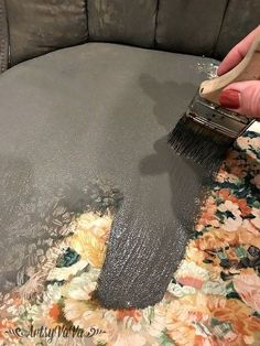 someone using a brush to paint a gray couch with floral fabric on the back and sides