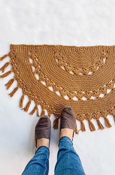 someone is standing on the floor next to a crocheted rug with fringes