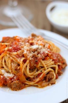 a white plate topped with spaghetti covered in sauce and meat next to a bowl of cheese