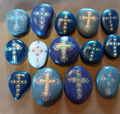 nine painted rocks with cross designs on them, all in different colors and sizes are shown