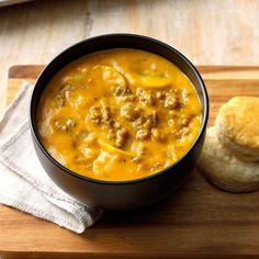 a bowl of soup next to a roll on a cutting board