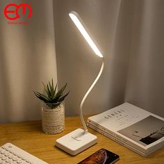 a desk lamp sitting on top of a wooden table next to a keyboard and phone