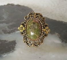 Unakite Ring This beautiful gold plated ring has a unakite stone setting and rhinestone accents. Adjustable band. art deco victorian edwardian art nouveau renaissance medieval boho bohemian style Gold Bohemian Filigree Rings, Bohemian Gold Filigree Rings, Victorian Gold Jewelry With Stone Setting, Vintage Crystal Ring With Cabochon, Vintage Gold Oval Crystal Ring, Antique Gold Crystal Gemstone Ring, Vintage Brass Rings With Intricate Design, Vintage Brass Cabochon Rings, Bohemian Gold Crystal Ring In Brass