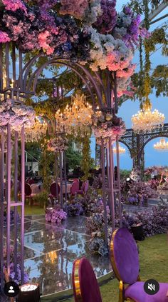 an outdoor event with purple chairs and chandeliers hanging from the ceiling, surrounded by flowers