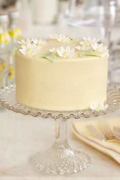 a cake with white flowers on it is sitting on a glass platter next to plates and napkins