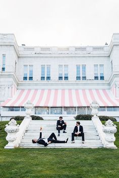 two men sitting on steps in front of a large building with pink and white striped awning