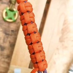 an orange paracording rope hanging from a hook on a wooden door handle with a green keychain in the background