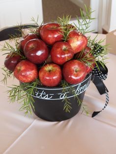 a black bucket filled with red apples on top of a white tablecloth covered table