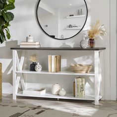 a white shelf with books and vases on it in front of a round mirror