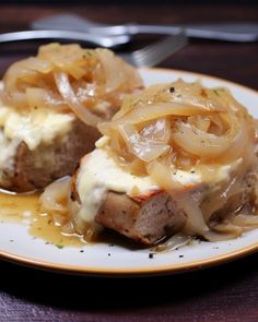 two meatballs covered in onions on a plate with gravy and a fork