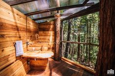 a bathroom with wooden walls and flooring surrounded by trees in the background is an outdoor jacuzzi tub