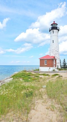 a light house sitting on top of a lush green field next to the ocean in front of a blue sky with white clouds