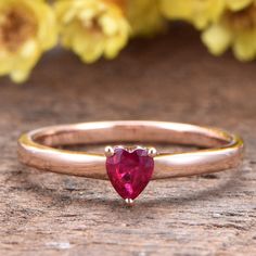 a pink heart shaped stone ring sitting on top of a wooden table next to yellow flowers