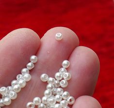 small white pearls are being held in the palm of a person's hand on a red background