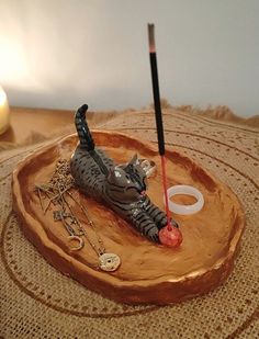 a cat figurine laying on top of a wooden tray next to a candle