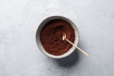 a bowl filled with cocoa powder and a spoon in the bowl next to it on a gray surface