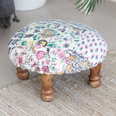 the foot stool is covered with a colorful flowered fabric and wooden legs, along with a potted palm tree in the background