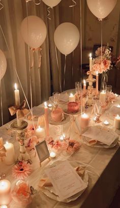 a table topped with lots of white balloons and plates filled with cake next to candles