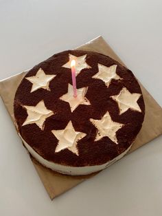 a chocolate cake with white stars and a single lit candle on top, sitting on a napkin