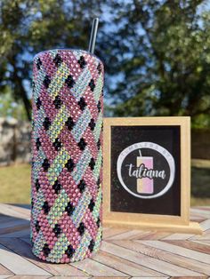 a pink and black cup sitting on top of a wooden table next to a sign