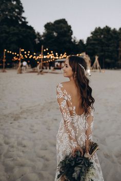 a woman standing on top of a sandy beach holding a bouquet in front of her