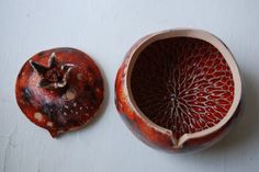 a red vase sitting on top of a white table next to a piece of fruit